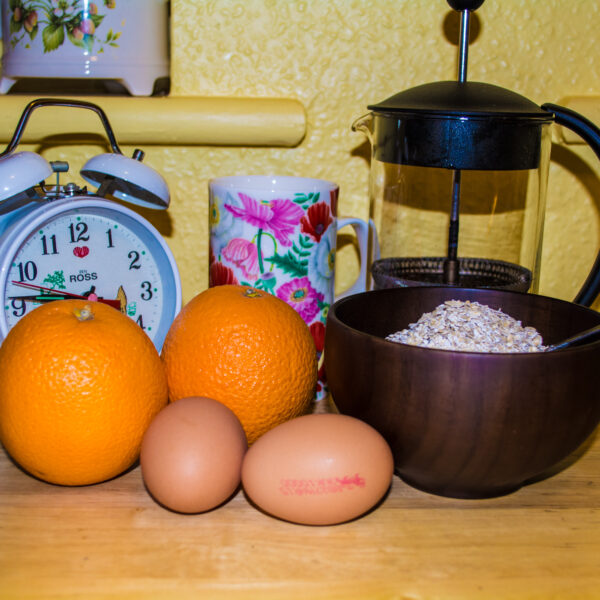 Breakfast; Alarm Clock, Coffee Mug, French Press, Oranges, Eggs, Porridge Oats in Wooden Bowl