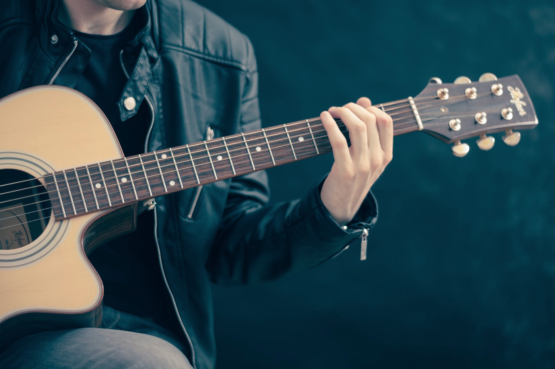 Man in a leather jacket playing acoustic guitar