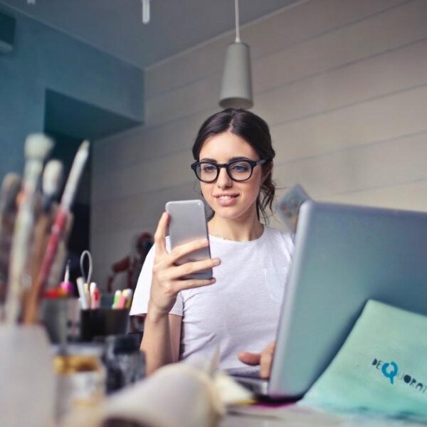 Young creative woman using a phone in front of a laptop