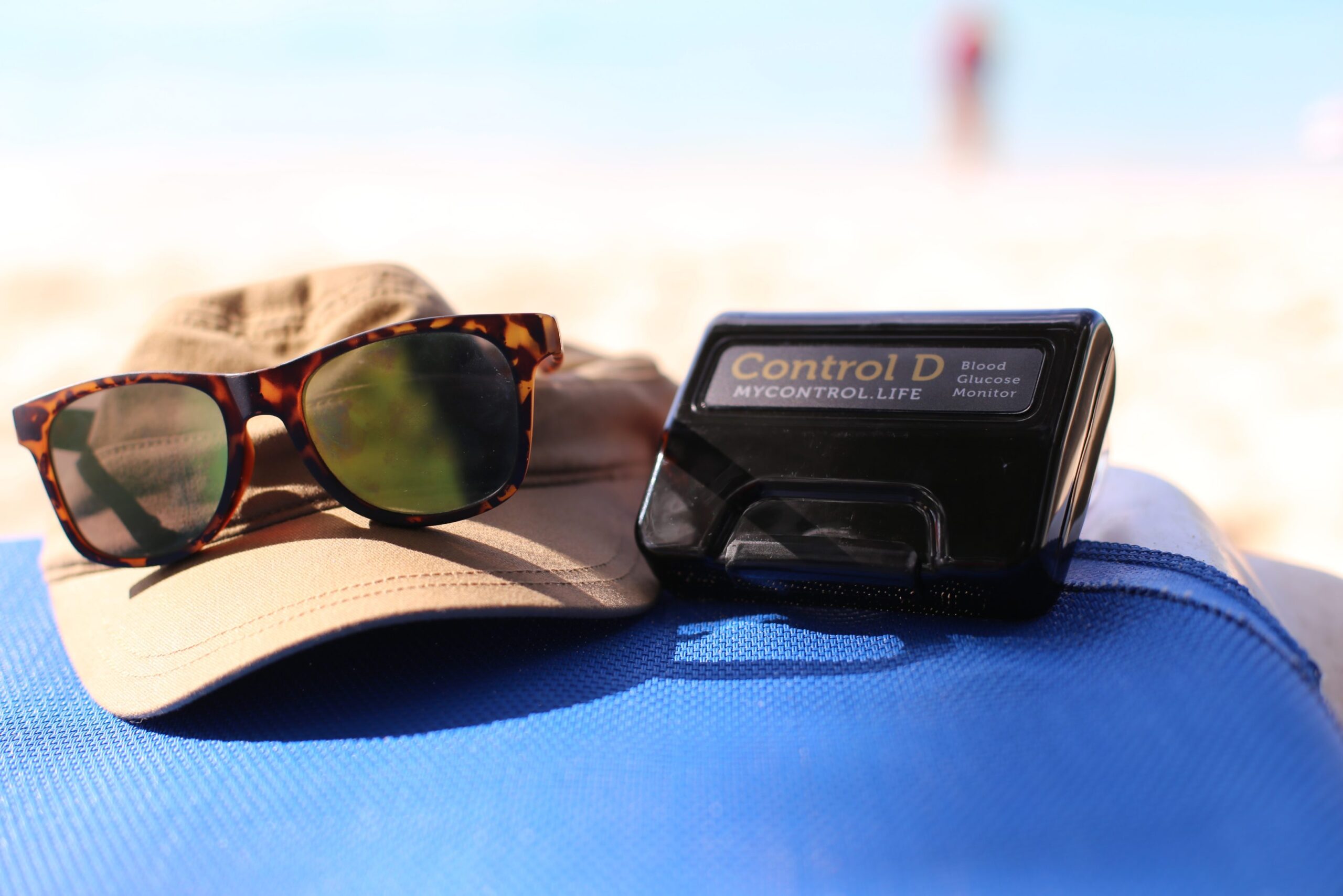 Control D Blood Glucose Monitor on the beach with hat and sunglasses