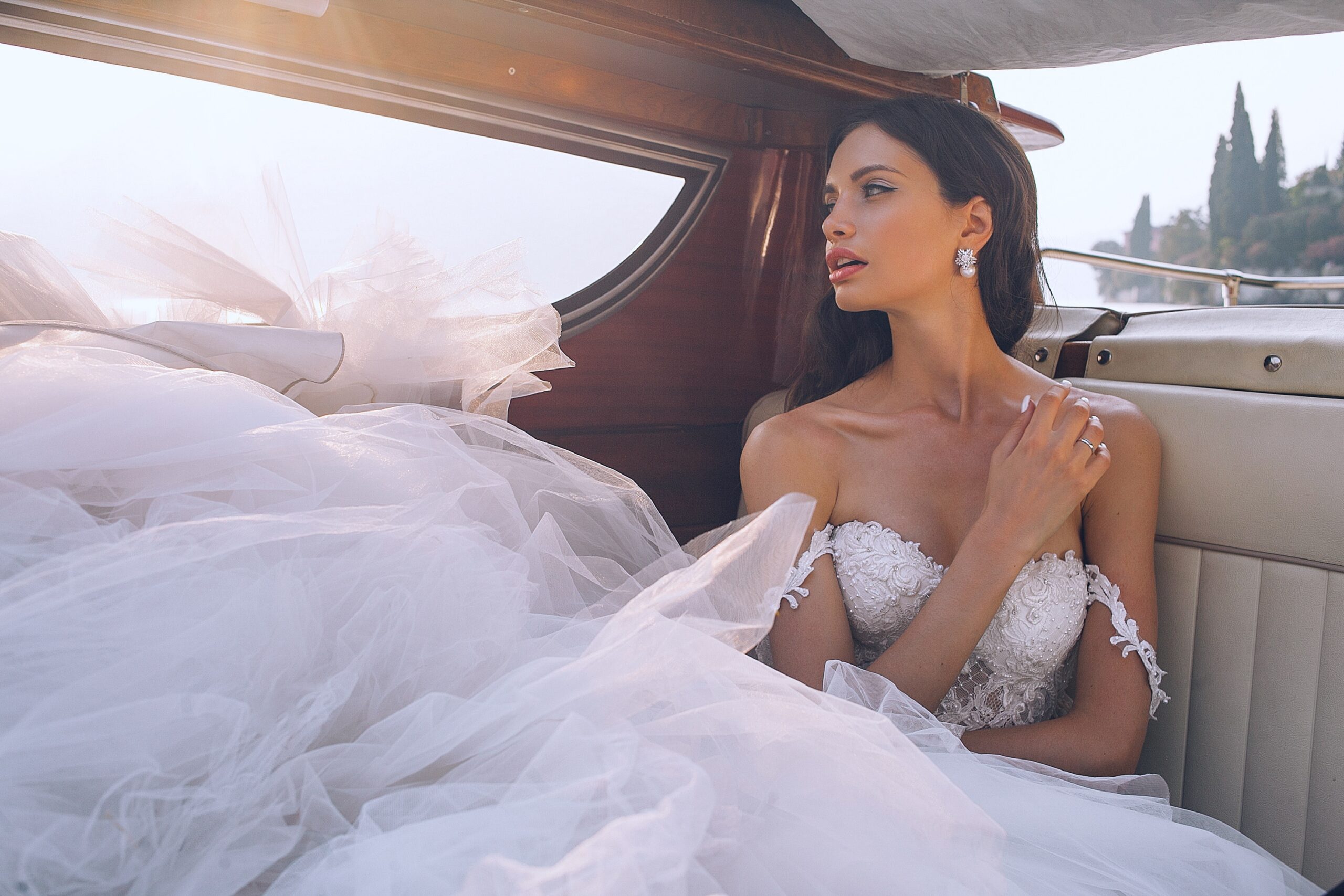 Bride wearing white sweetheart-neckline wedding dress inside vehicle