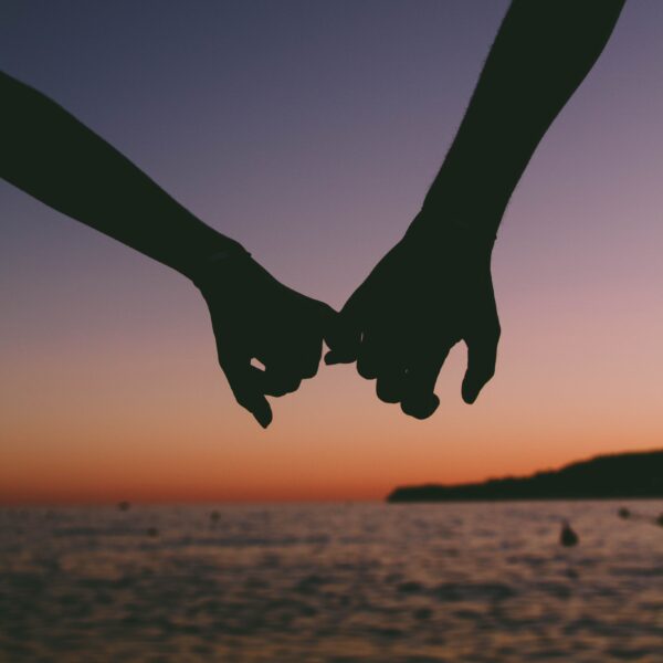 Two people holding pinkies on the beach