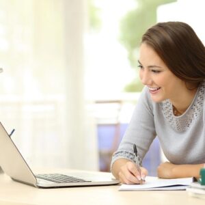 Woman smiling whilst copying information down from a laptop