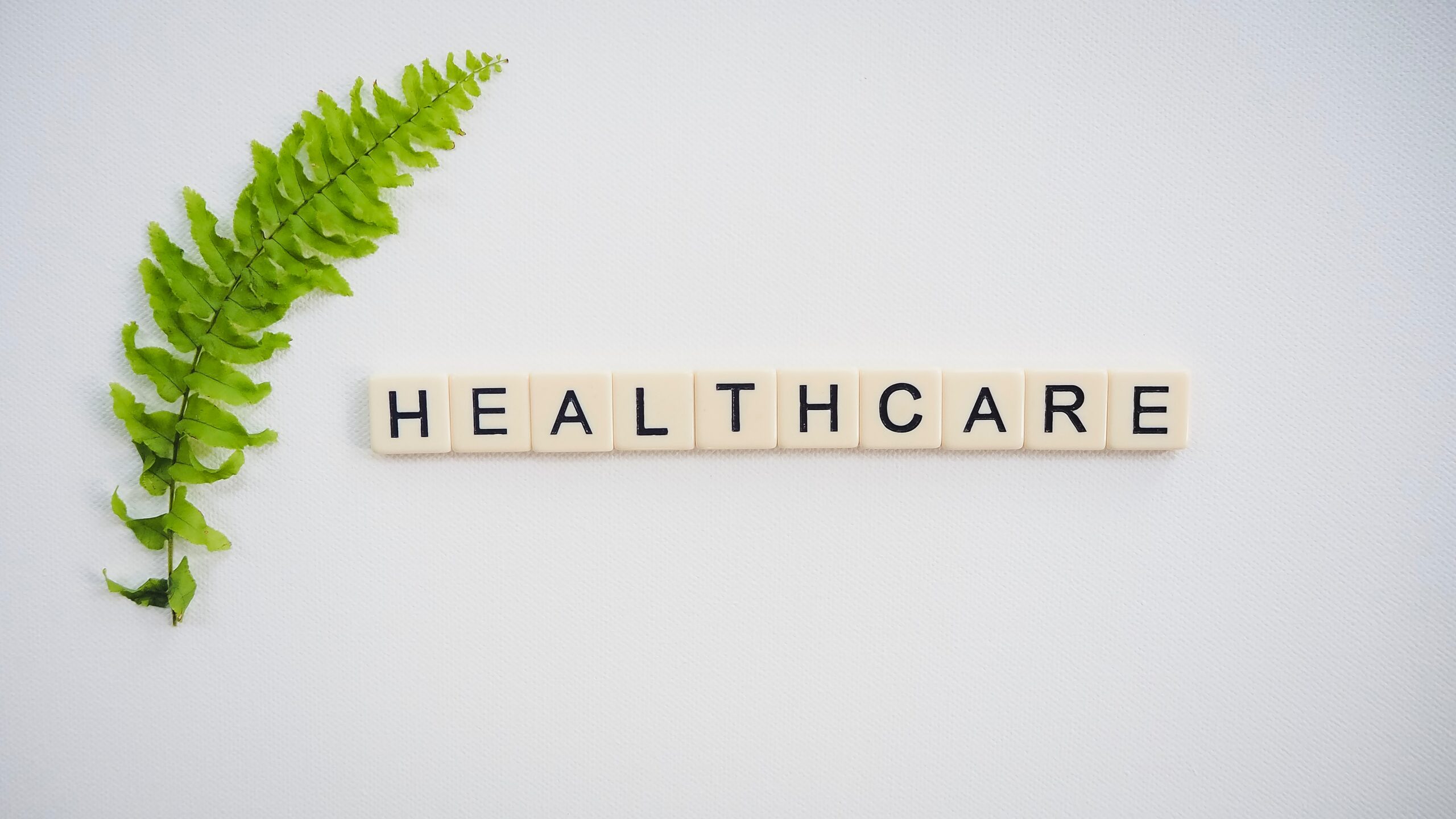 Scrabble pieces spelling out 'healthcare' next to a leaf