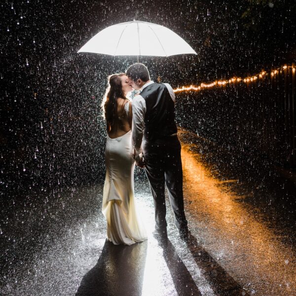 Bride and groom kissing under umbrella in the rain
