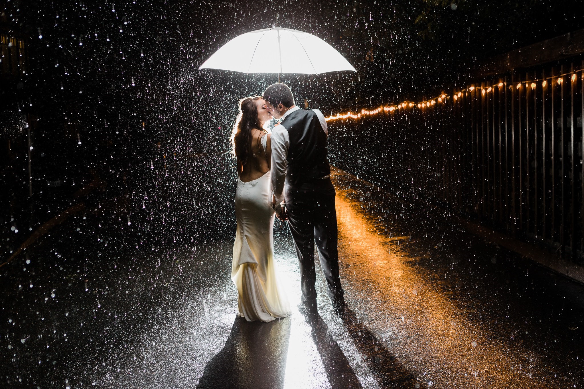 Bride and groom kissing under umbrella in the rain