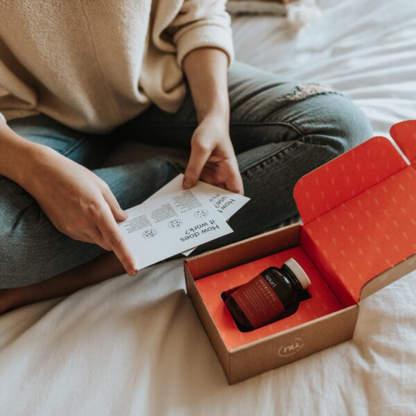 Woman sitting on bed while reading package materials included within the Nouri subscription box