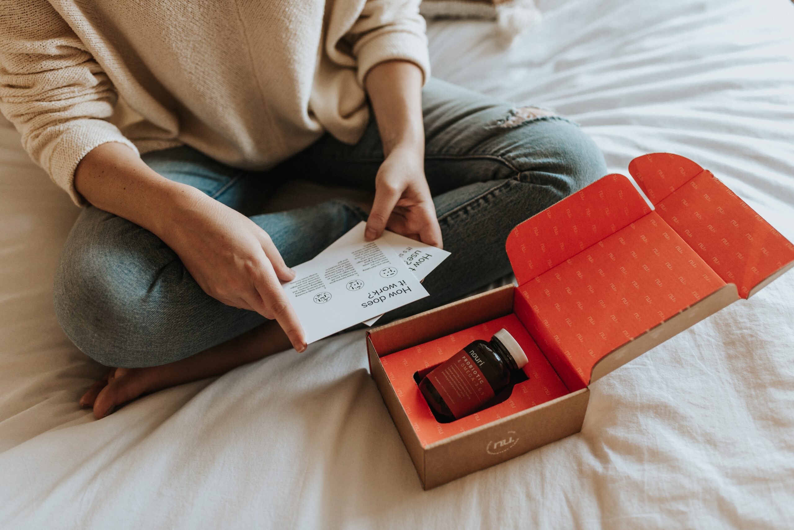 Woman sitting on bed while reading package materials included within the Nouri subscription box