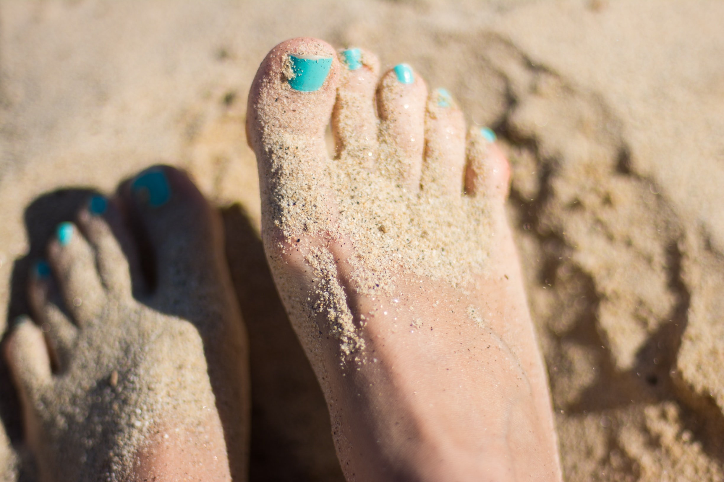 Feet with painted nails covered in sand