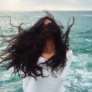 Woman standing near water with her hair being blown into her face