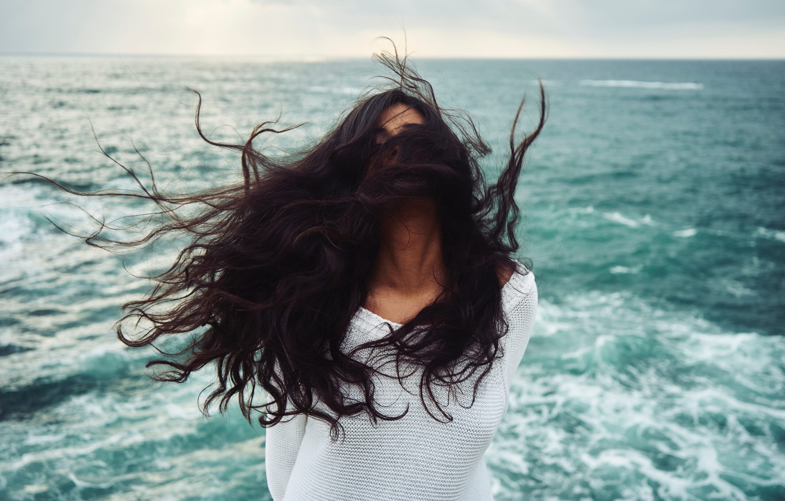 Woman standing near water with her hair being blown into her face