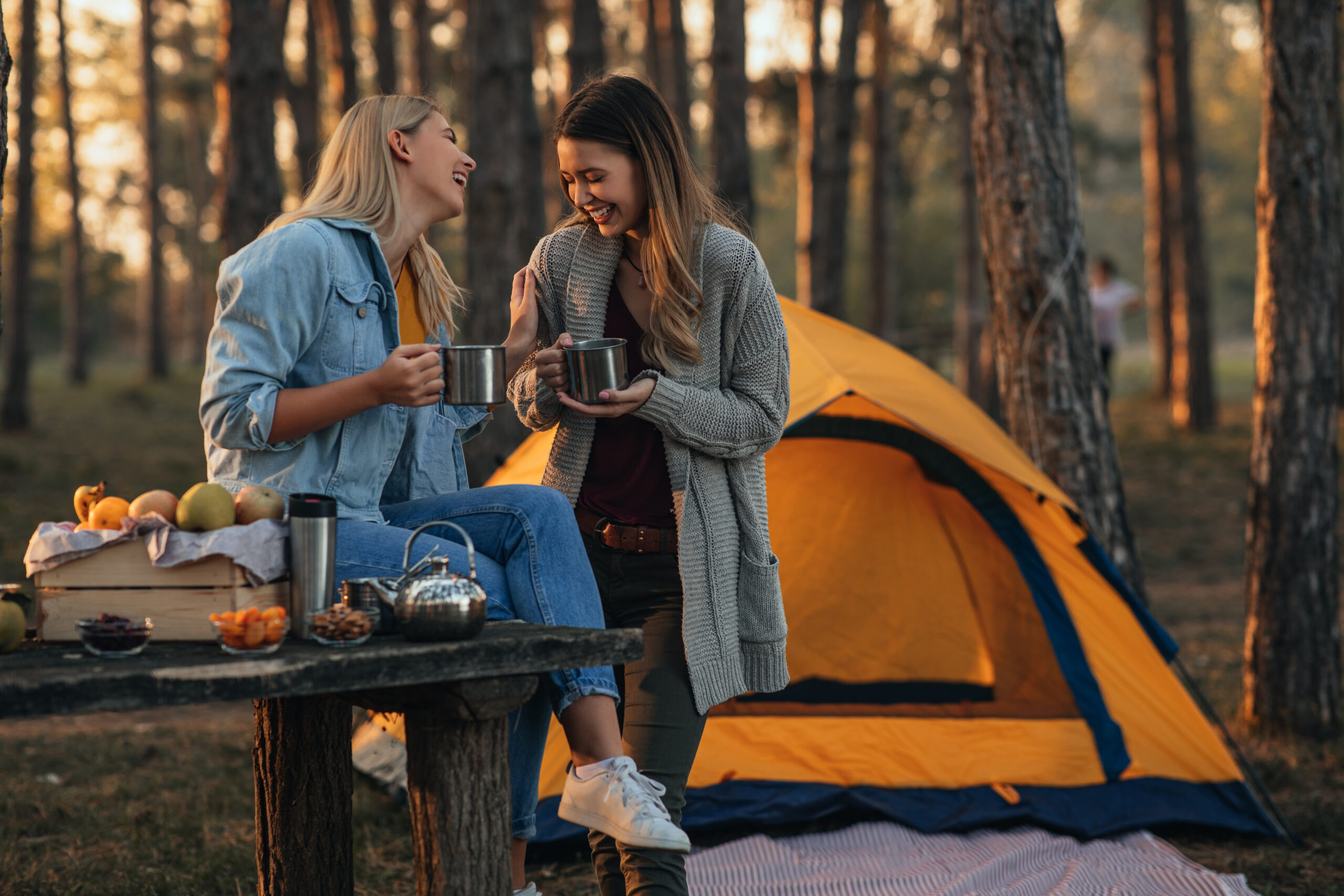 Young women enjoying hot drink at the forest during autumn weekend