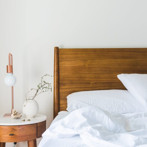 White bedspread, beside nightstand with a copper table lamp on it