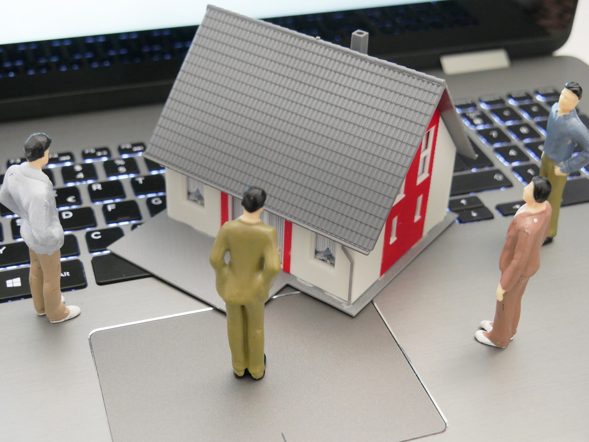 A model house and people figurines on top of a laptop keyboard