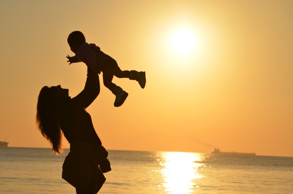 Woman carrying baby at the beach during sunset