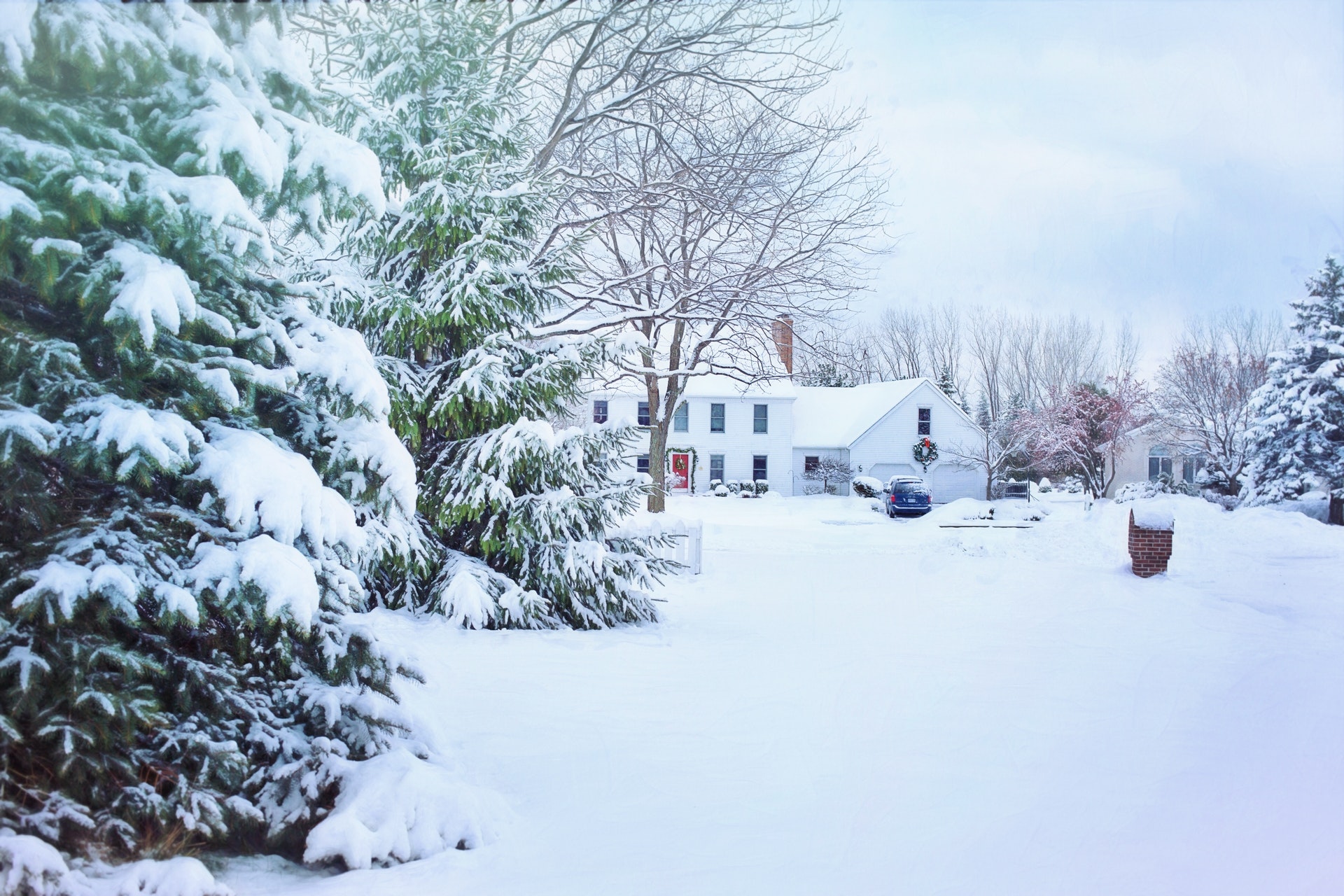 A house surrounded by snow with trees in the foreground