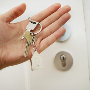 Hand in front of door holding keys with a house keychain on it