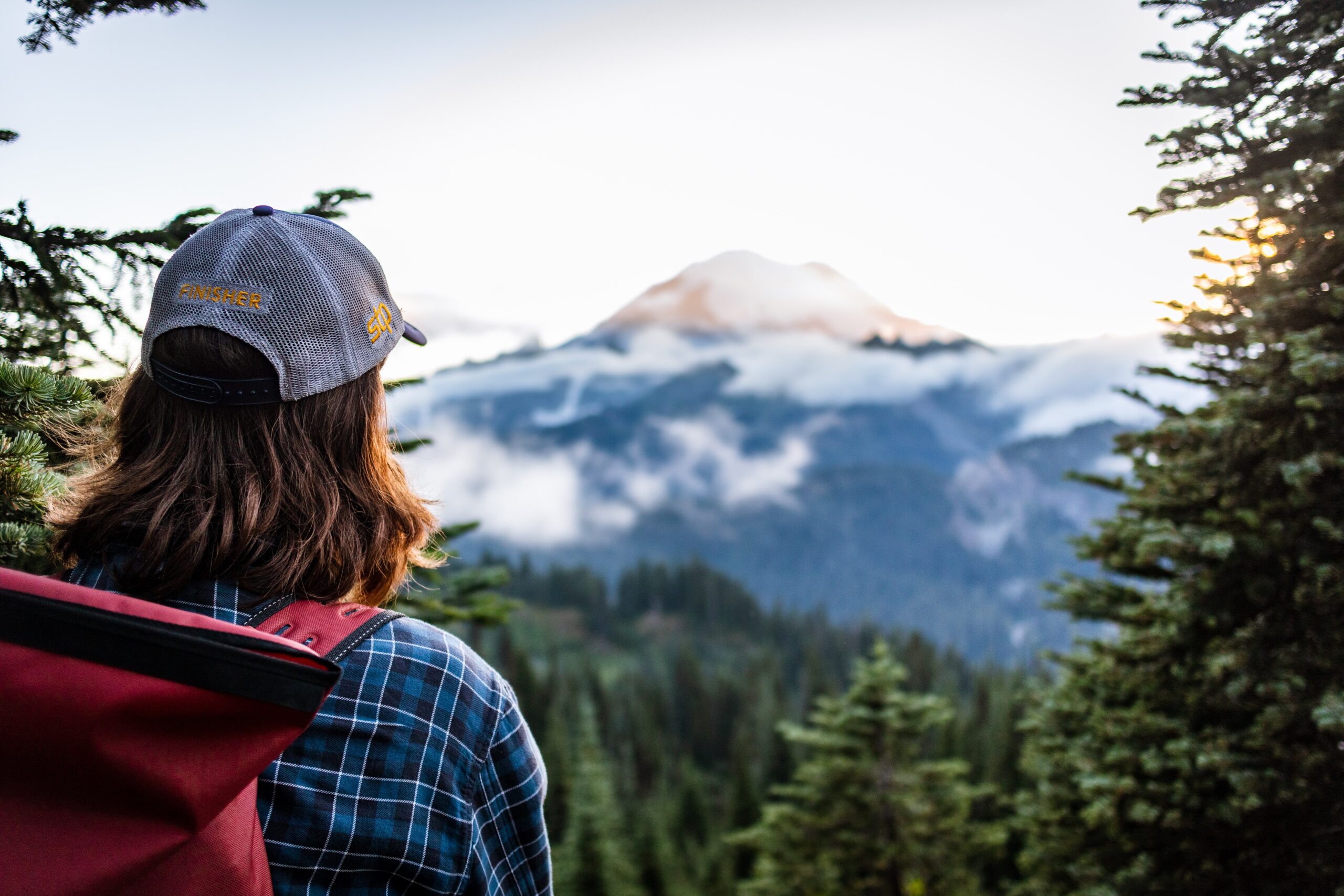 Young hiker overlooks the sunsetting on Mount Rainier wearing a Seattle to Portland biker's trucker-cap and hiking bag