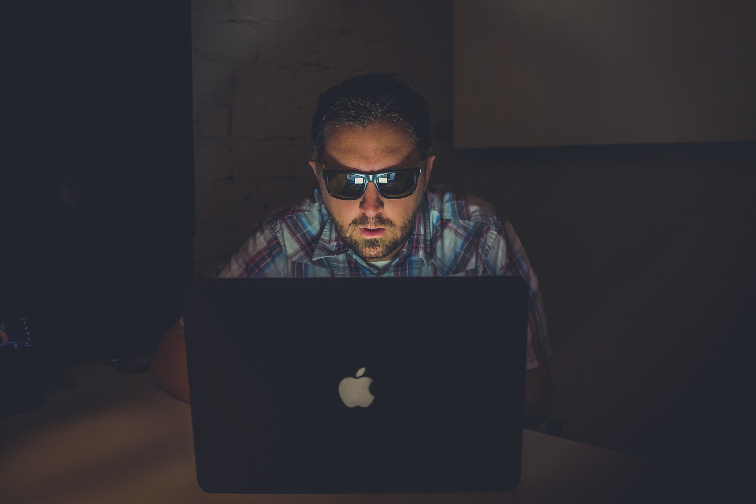 Man wearing sunglasses in front of a laptop in a dark room