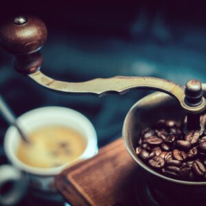 A coffee grinder full of beans with a cup of coffee in the background