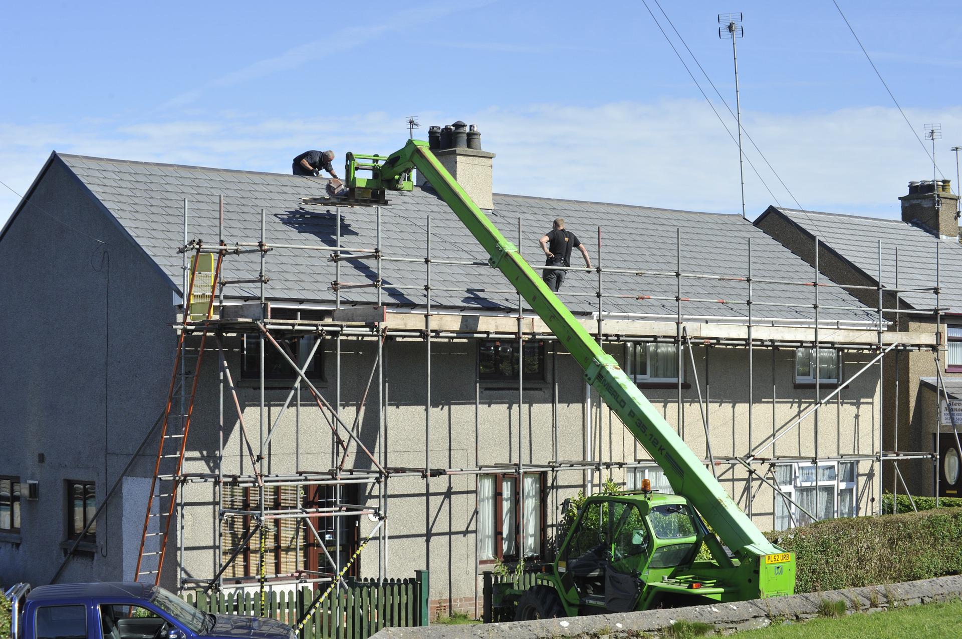 Roofers using and scaffolding crane to repair roof tiles