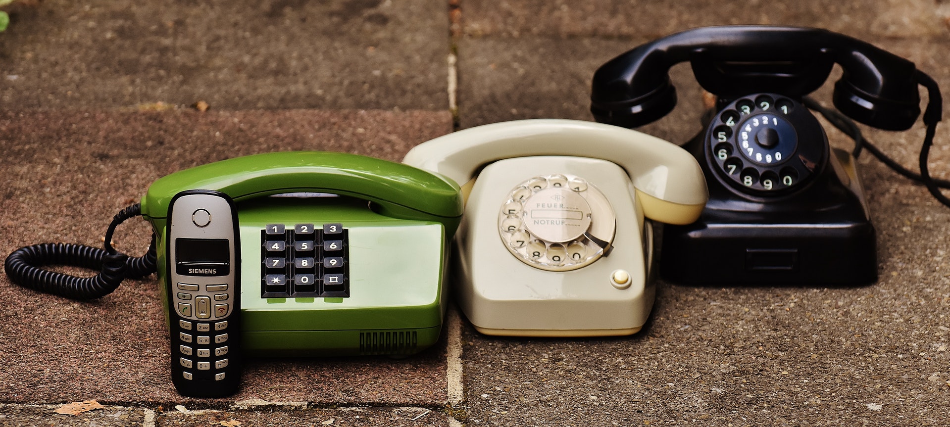 Three rotary telephones and a mobile phone