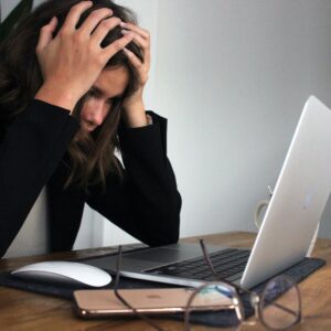 Woman sitting in front of a laptop with her hands on her head