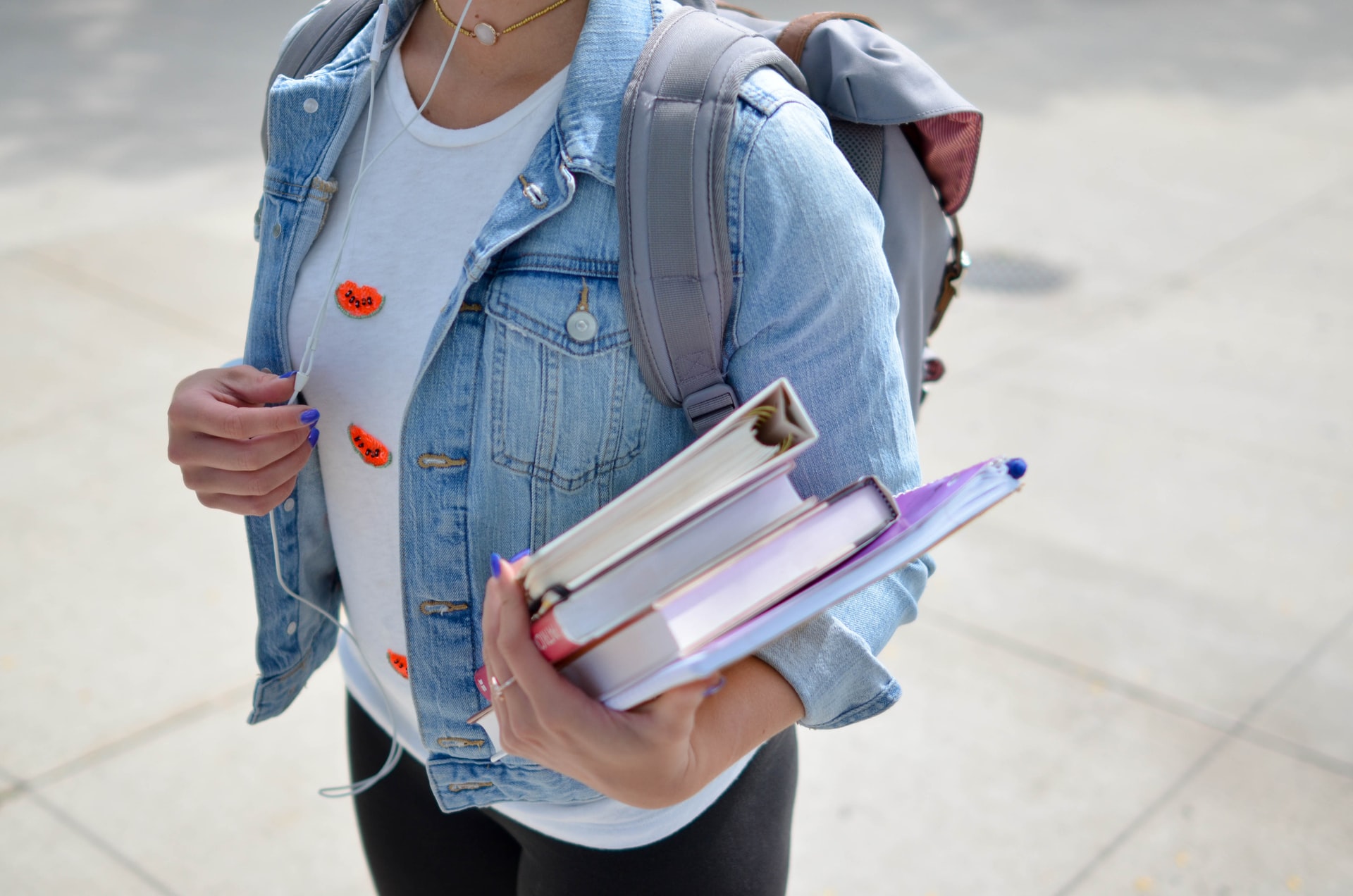 Woman wearing denim jacket and earbuds, carrying books