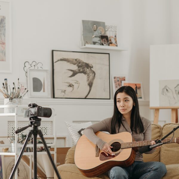 Woman playing guitar in front of a camera on a tripod