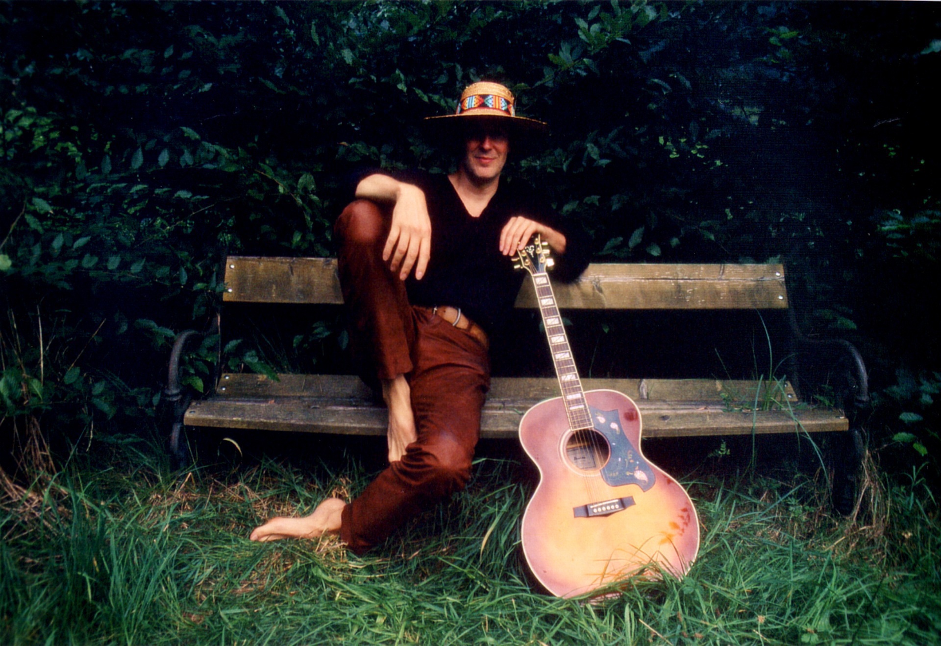 Man wearing brown leather trousers sitting on a bench and leaning on a guitar