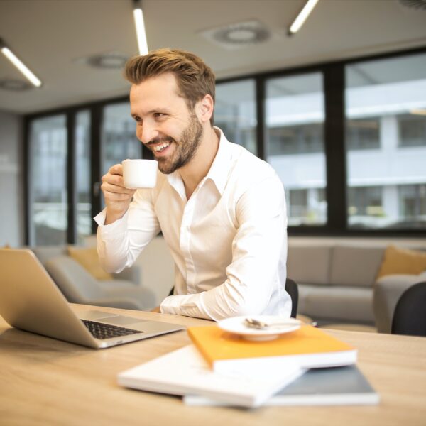 Man drinking a mug of coffee in front of a laptop