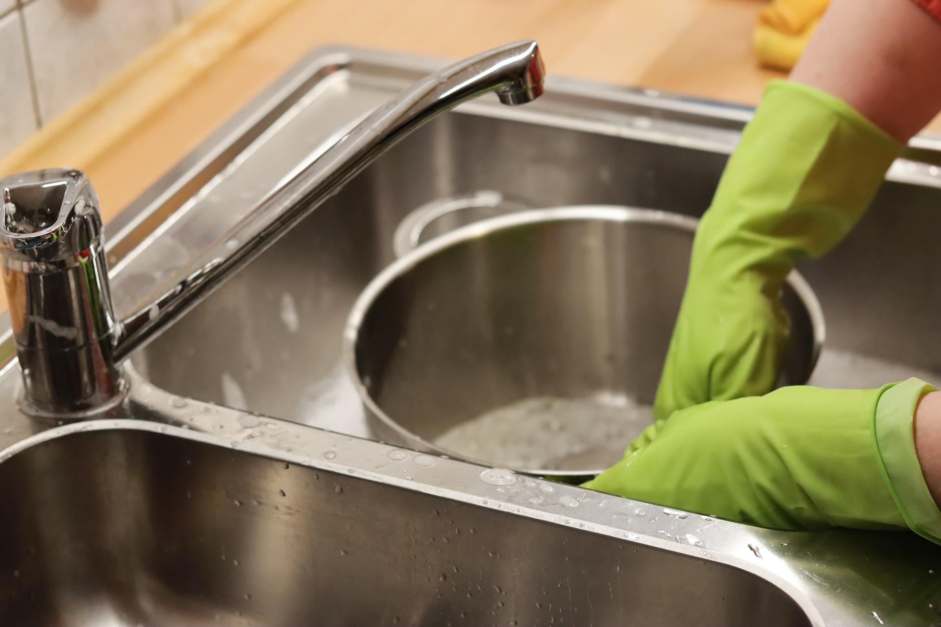 Person wearing green gloves and washing dishes