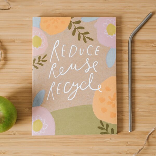 Floral notebook with the words "Reduce, Reuse, Recycle" written on the cover, with a metal straw, twine, and a green apple