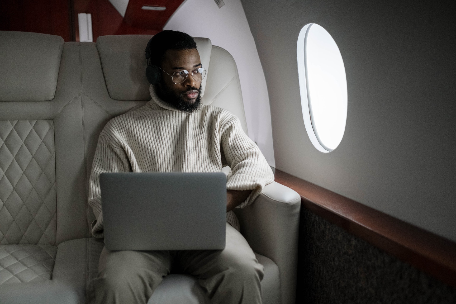 Man in tan sweater using a MacBook while sitting on a couch on an airplane