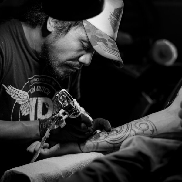 Greyscale photo of a man tattooing someone