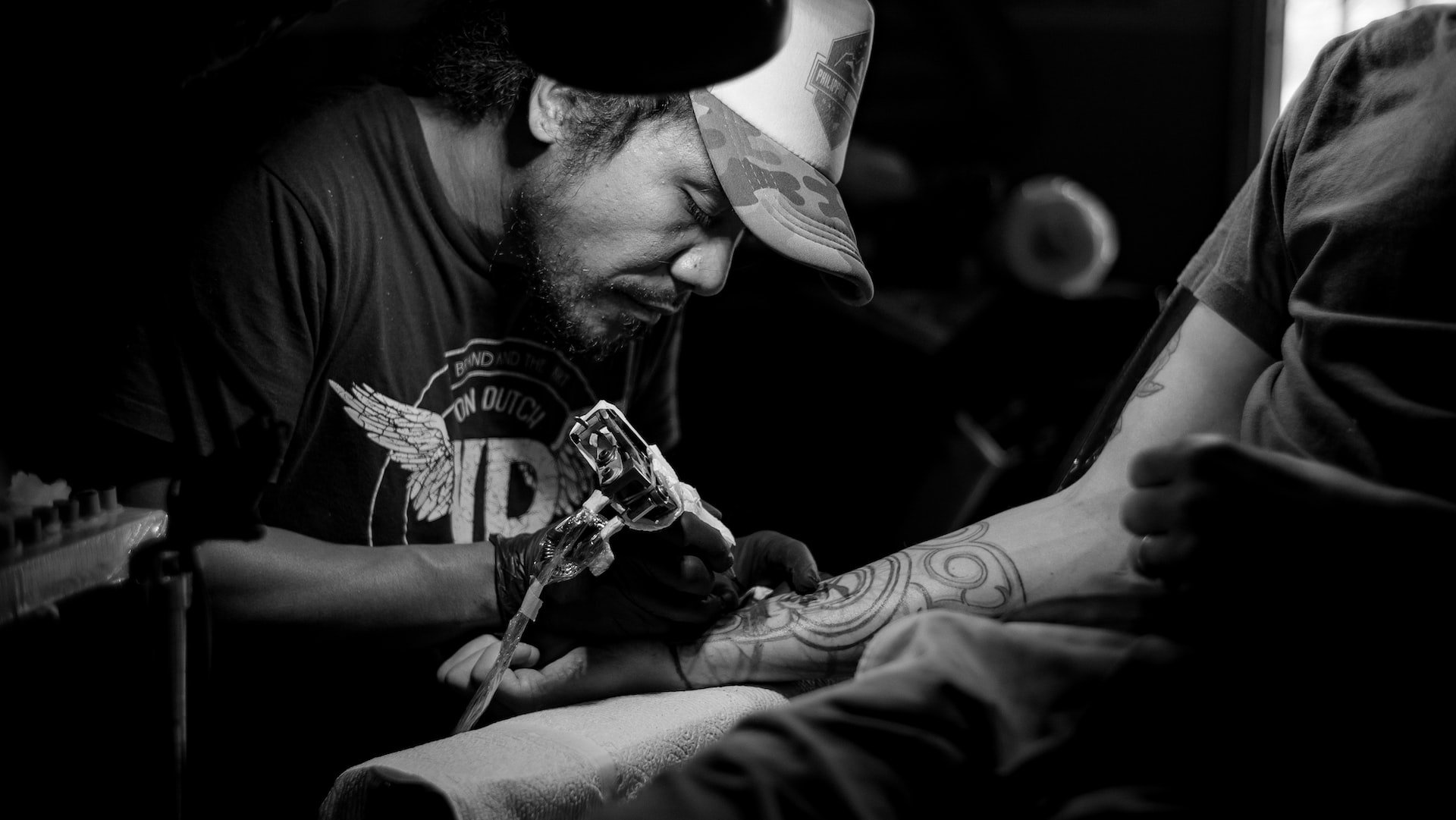 Greyscale photo of a man tattooing someone