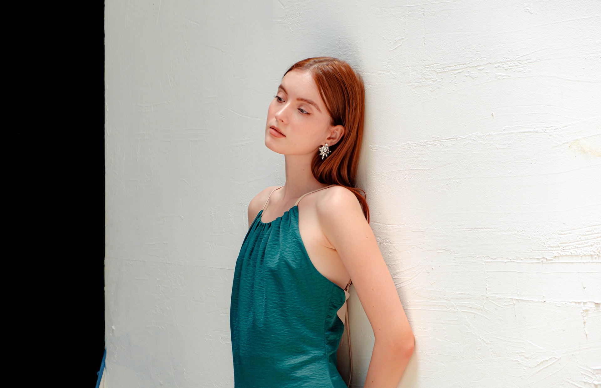 Girl with red hair in a green dress leaning against a wall