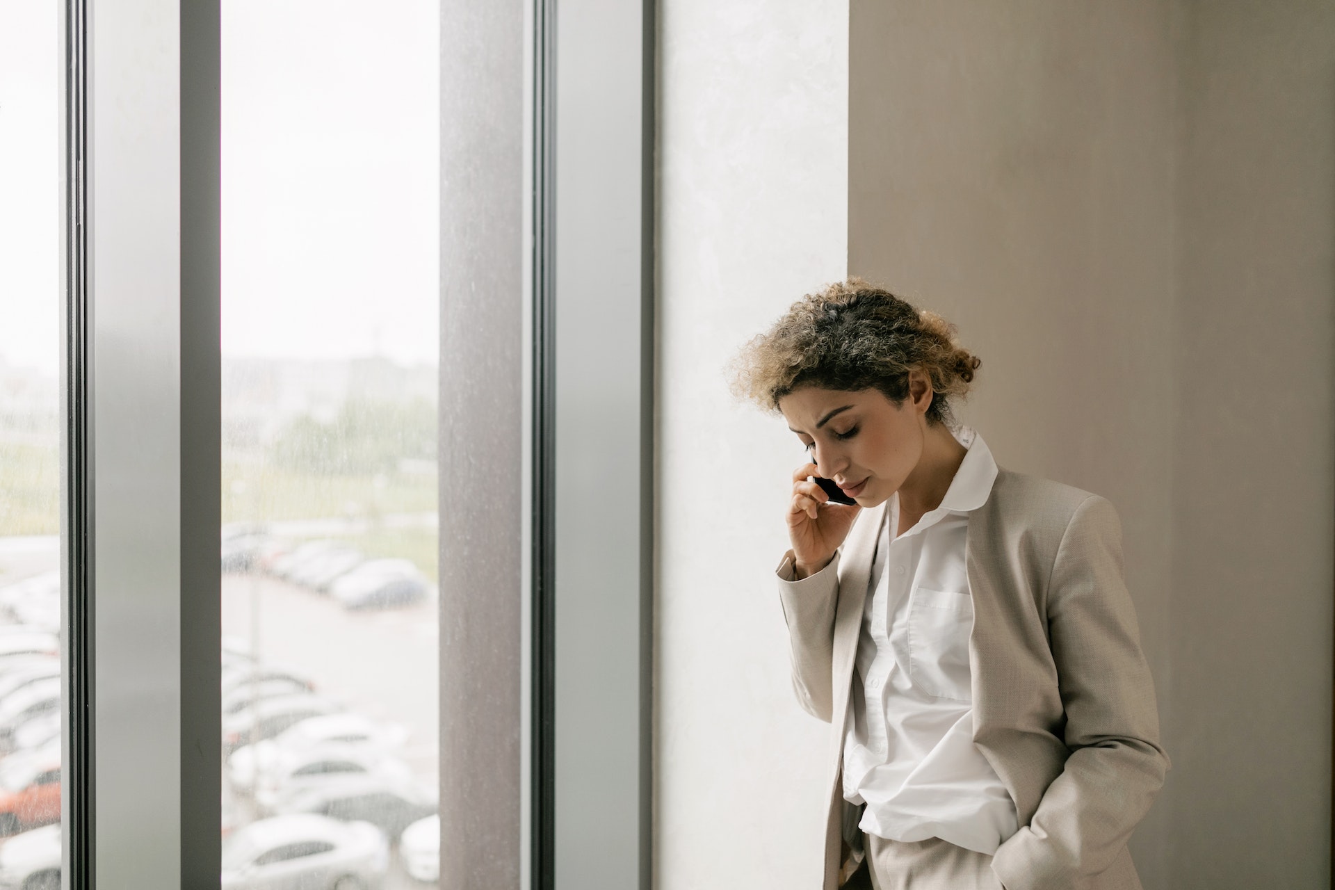 A Woman Standing Beside Window while Talking on the Phone