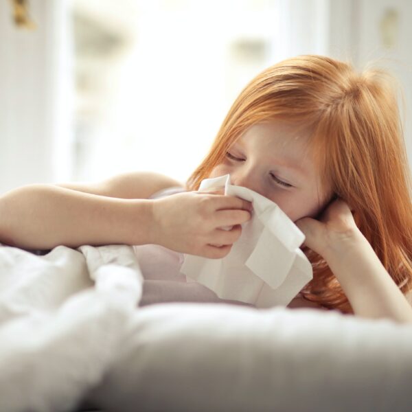 Sick girl wiping nose on a tissue whilst lying in bed