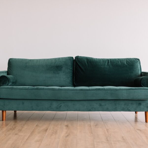 Cool hipster green couch sofa with brown wooden legs on wooden floor in front of a white wall