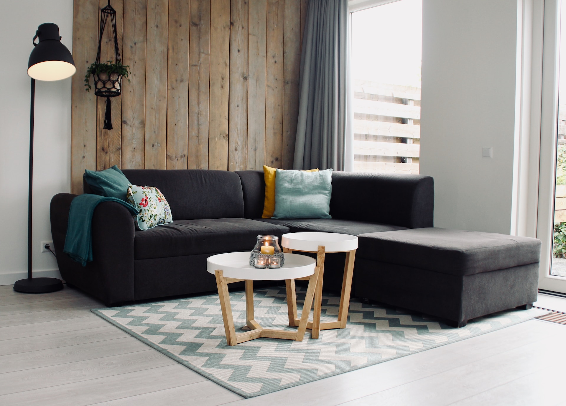 Black sofa with colourful cushions, a tall lamp, a wooden wall, and two coffee tables