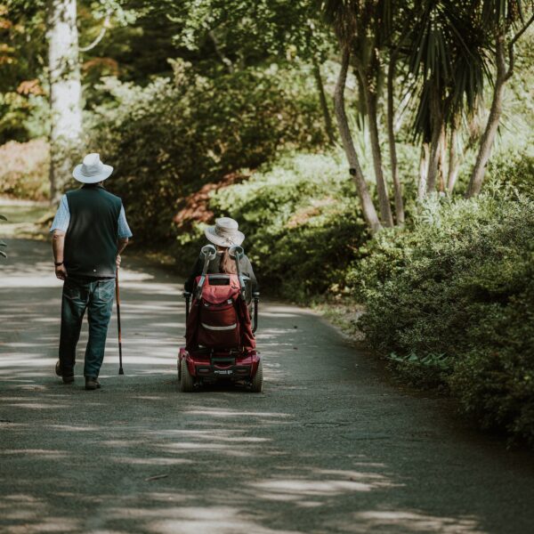 Man with a walking stick and woman in a wheelchair going down a path