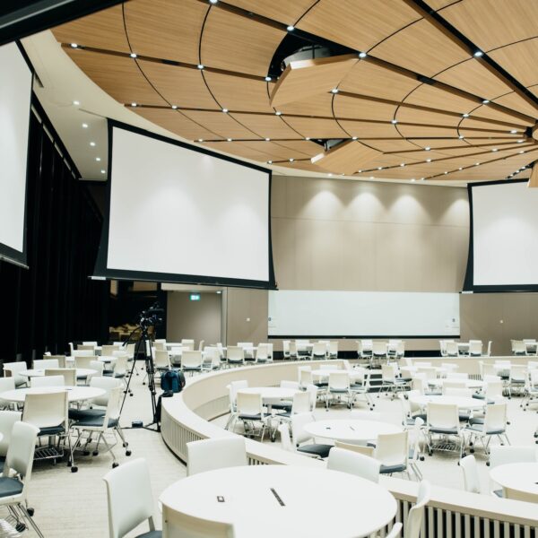 An empty room with white tables, chairs and projector screens