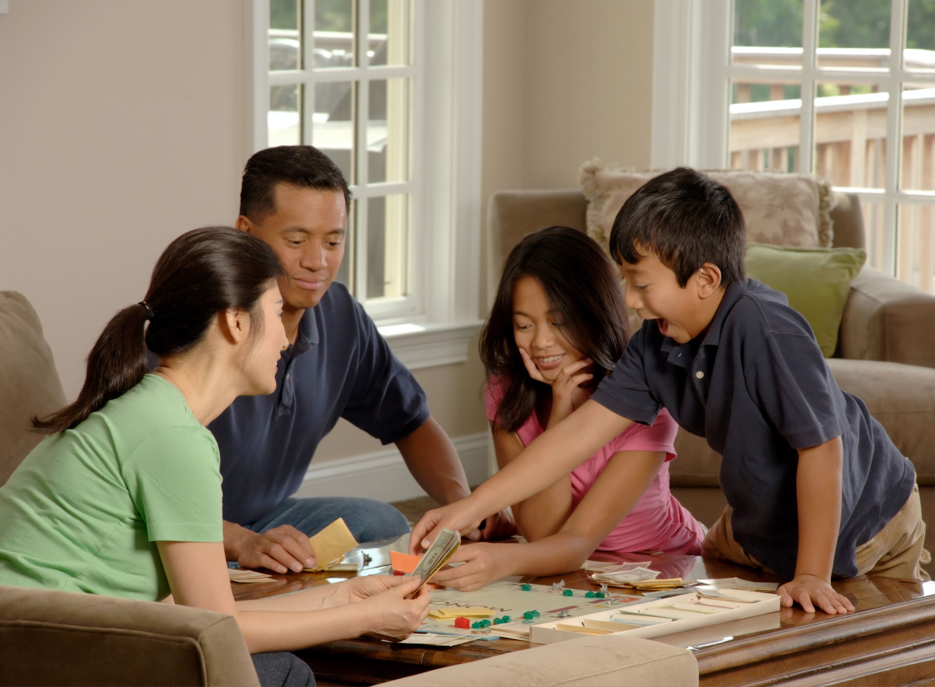 Two adults and two adolescents sitting around a coffee table playing Monopoly.