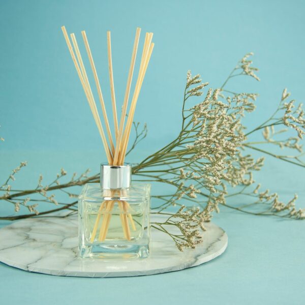 Glass of natural essential oil with sticks, with a white plant and blue background