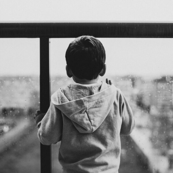 Greyscale photo of a child looking out of window on a rainy day