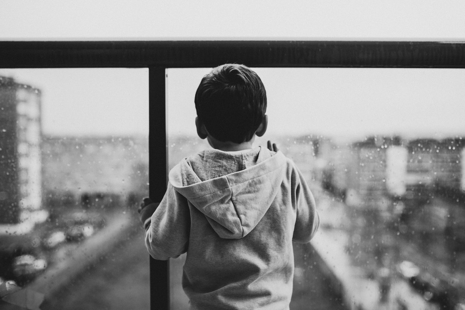Greyscale photo of a child looking out of window on a rainy day