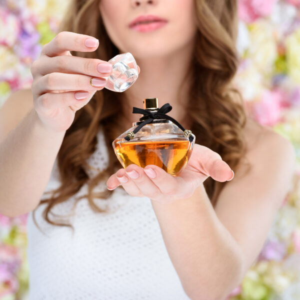 Woman opening bottle of perfume on floral background